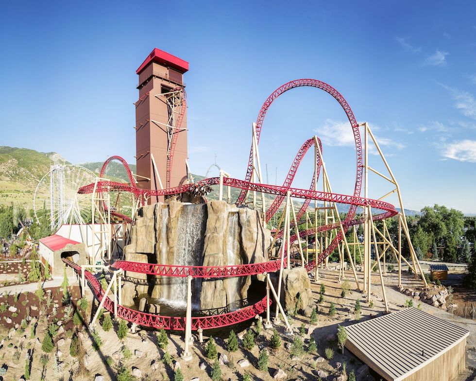 Cannibal, a red roller coaster with loops and a waterfall at Lagoon amusement park under a clear blue sky.