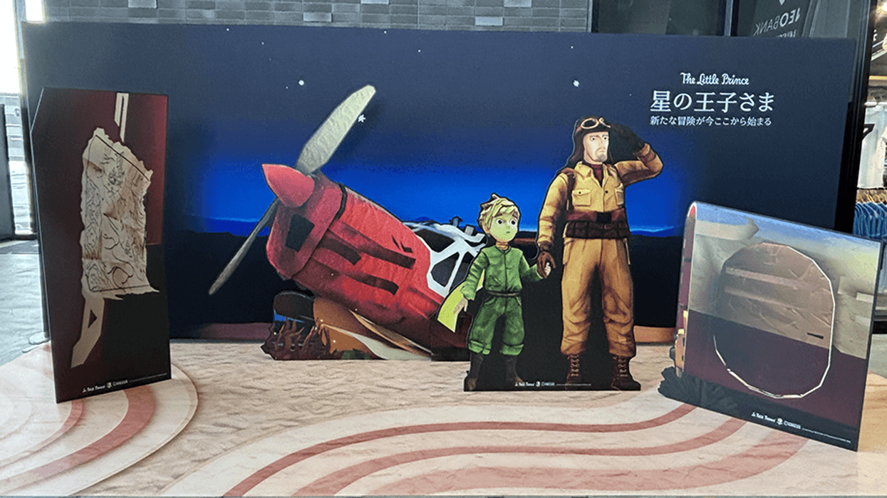 Cardboard cutouts of "The Little Prince" and pilot beside a red plane at a display.