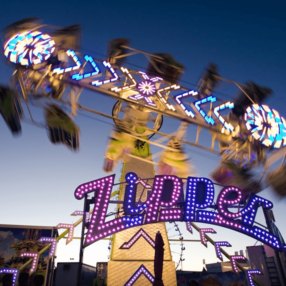 Carnival ride "Zipper" spinning with colorful lights against a twilight sky.