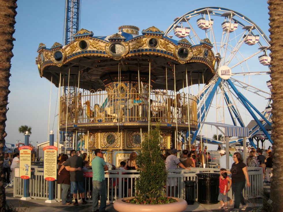 Carousel and Ferris wheel at a busy amusement park, with people gathered around.