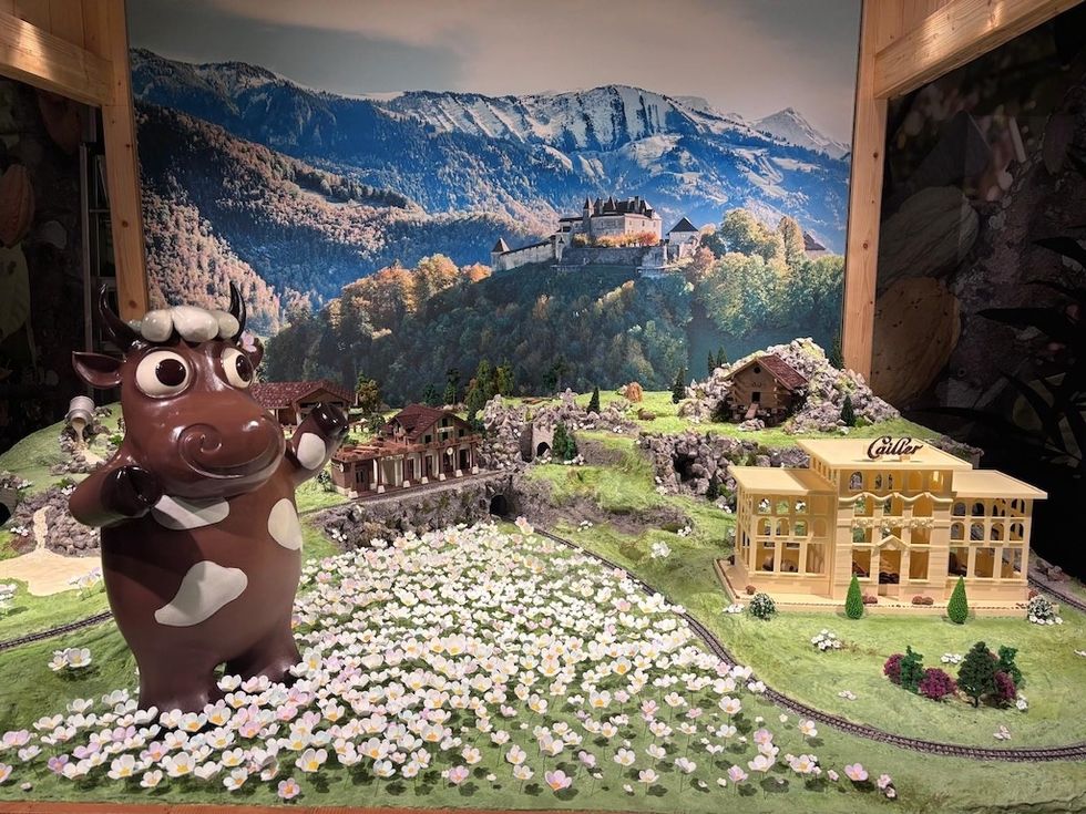 Cartoon cow statue in a mini alpine village diorama with a mountainous backdrop - exhibit at Maison Cailler