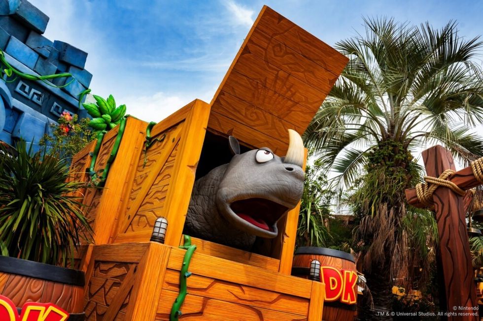 Cartoon rhino in wooden crate at amusement park area called Donkey Kong Country surrounded by tropical plants.