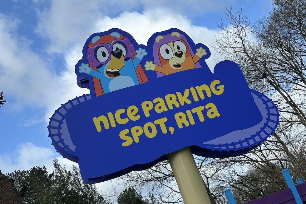 Cartoon sign with Bluey: "Nice Parking Spot, Rita" under a blue sky.