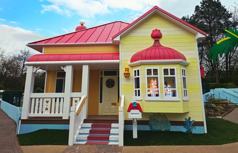 Cartoon-style yellow house with red roof and characters in the window.