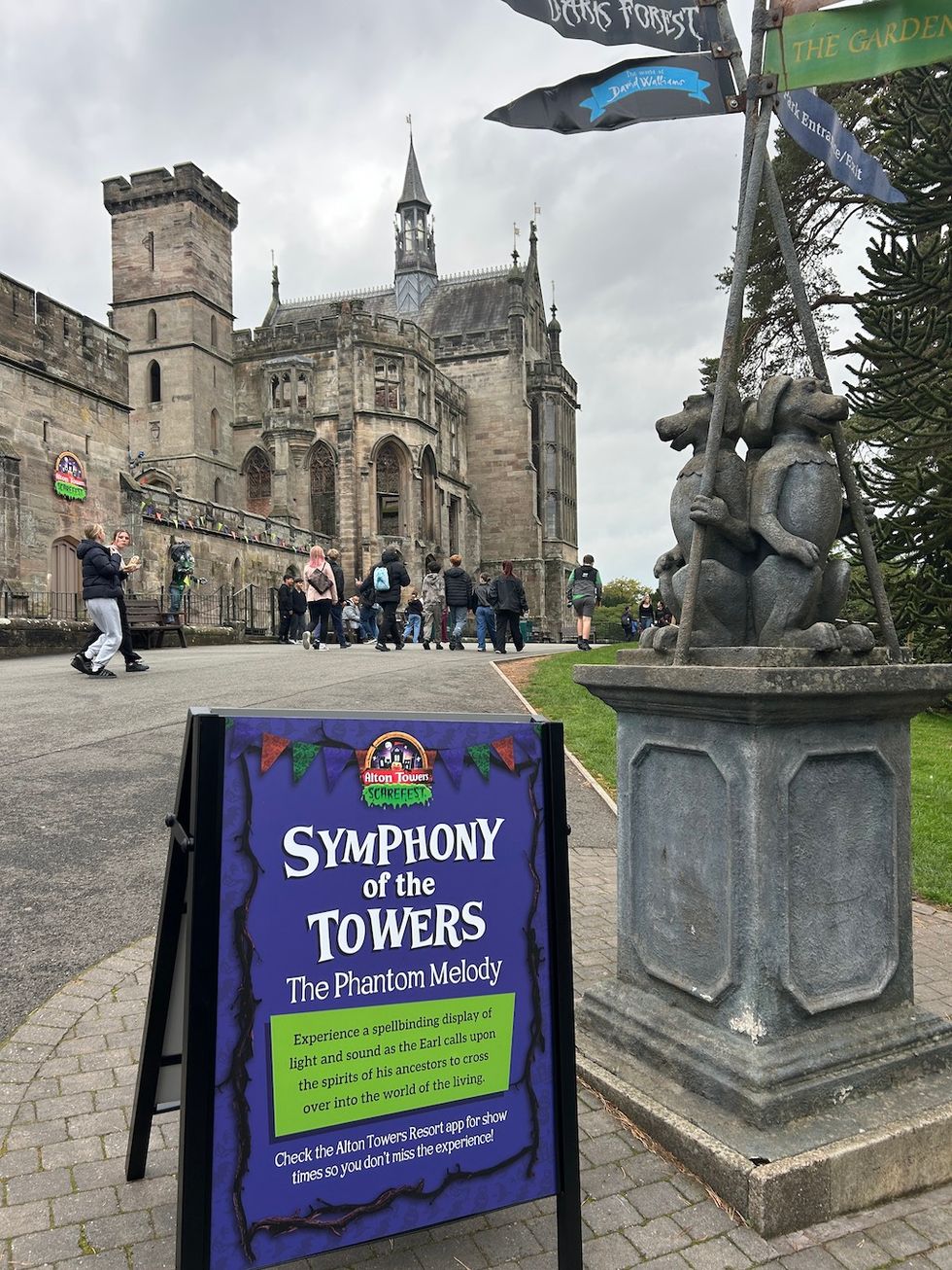 Castle entrance with sign for "Symphony of the Towers" event, people walking nearby.