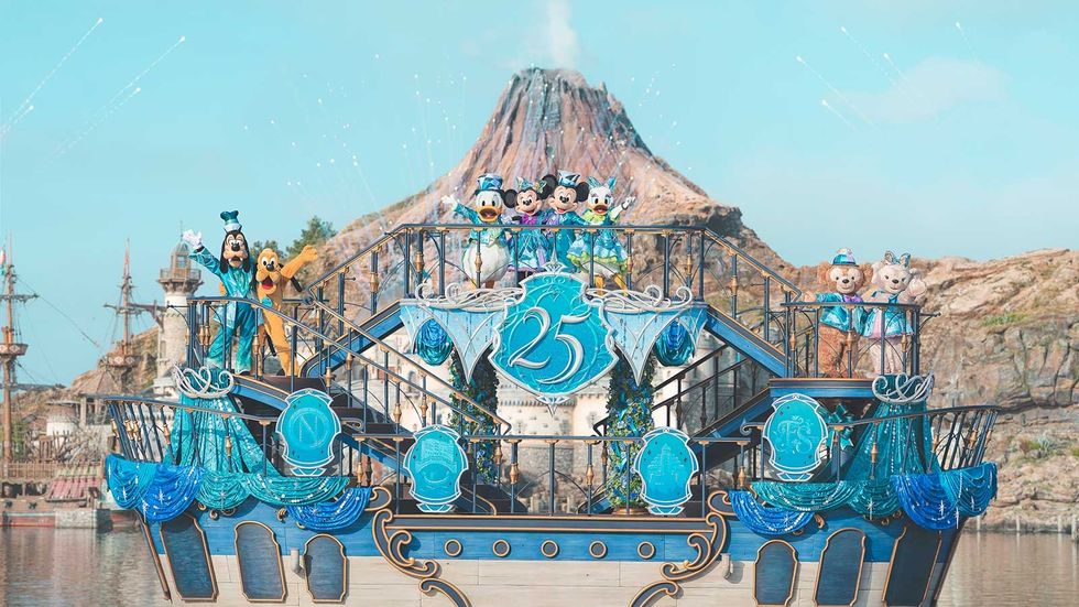 Characters in blue costumes on a ship, with a volcano backdrop, celebrating 25 years.