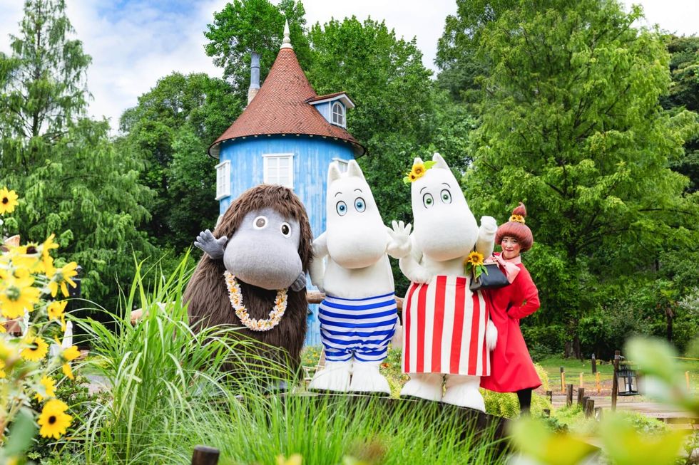 Characters pose in front of a blue house with lush greenery and sunflowers around.