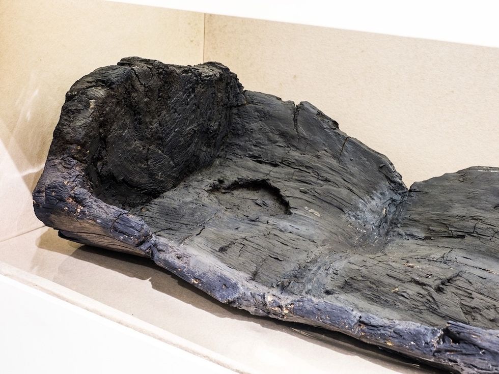 Charred wooden canoe with a circular hole in a display case.