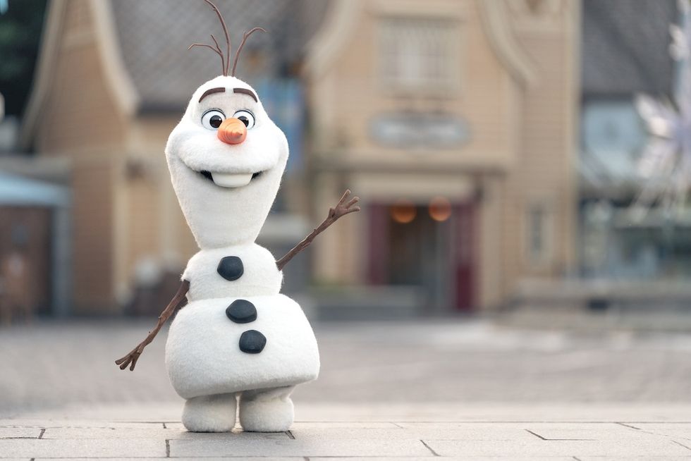 Cheerful Olaf snowman character with twig arms and carrot nose, standing outdoors.