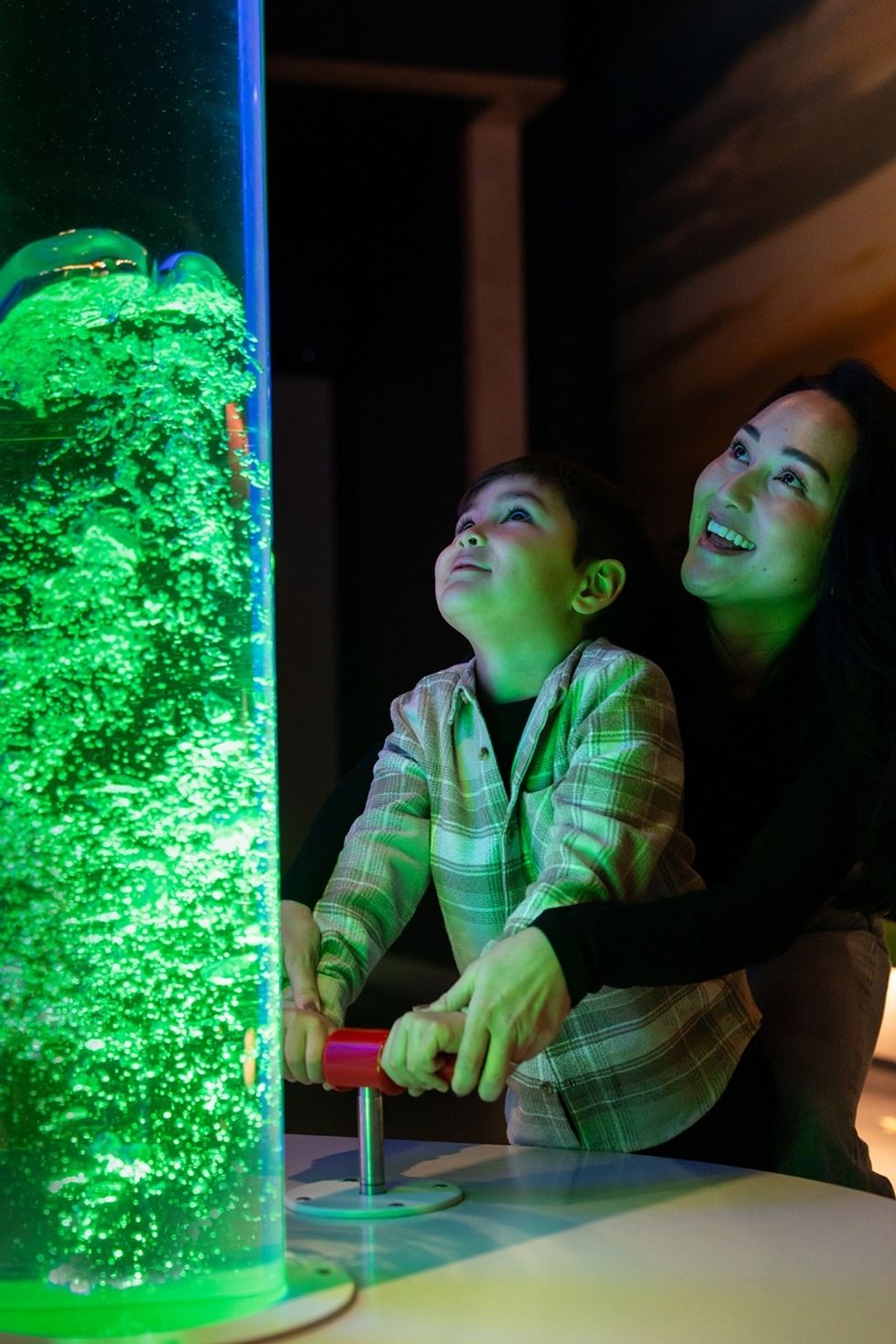 Child and adult interacting with a glowing green bubble tube exhibit at the International Centre for Life
