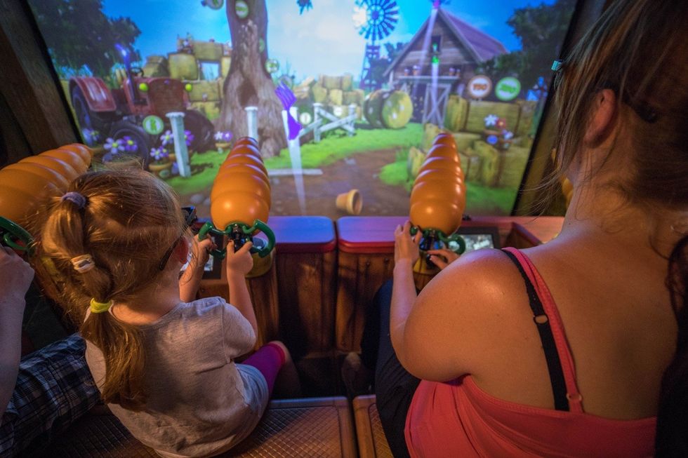 Child and adult playing an interactive farm-themed shooting game at an arcade.