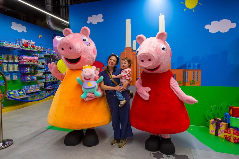 Child and adult posing with Peppa Pig characters in a colorful store setting.