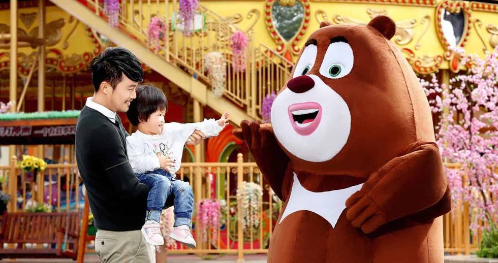 Child and parent meet a bear mascot at an amusement park.