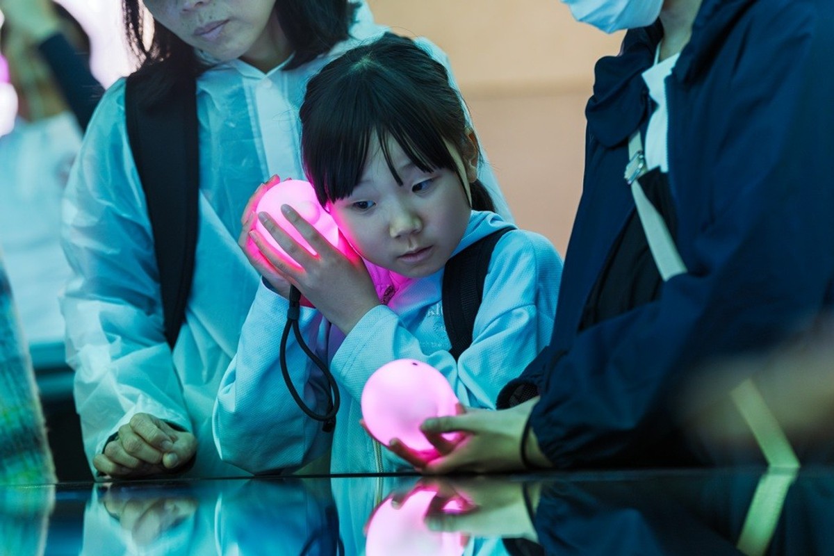 Child holding glowing orb, surrounded by adults in protective clothing at an interactive exhibit.