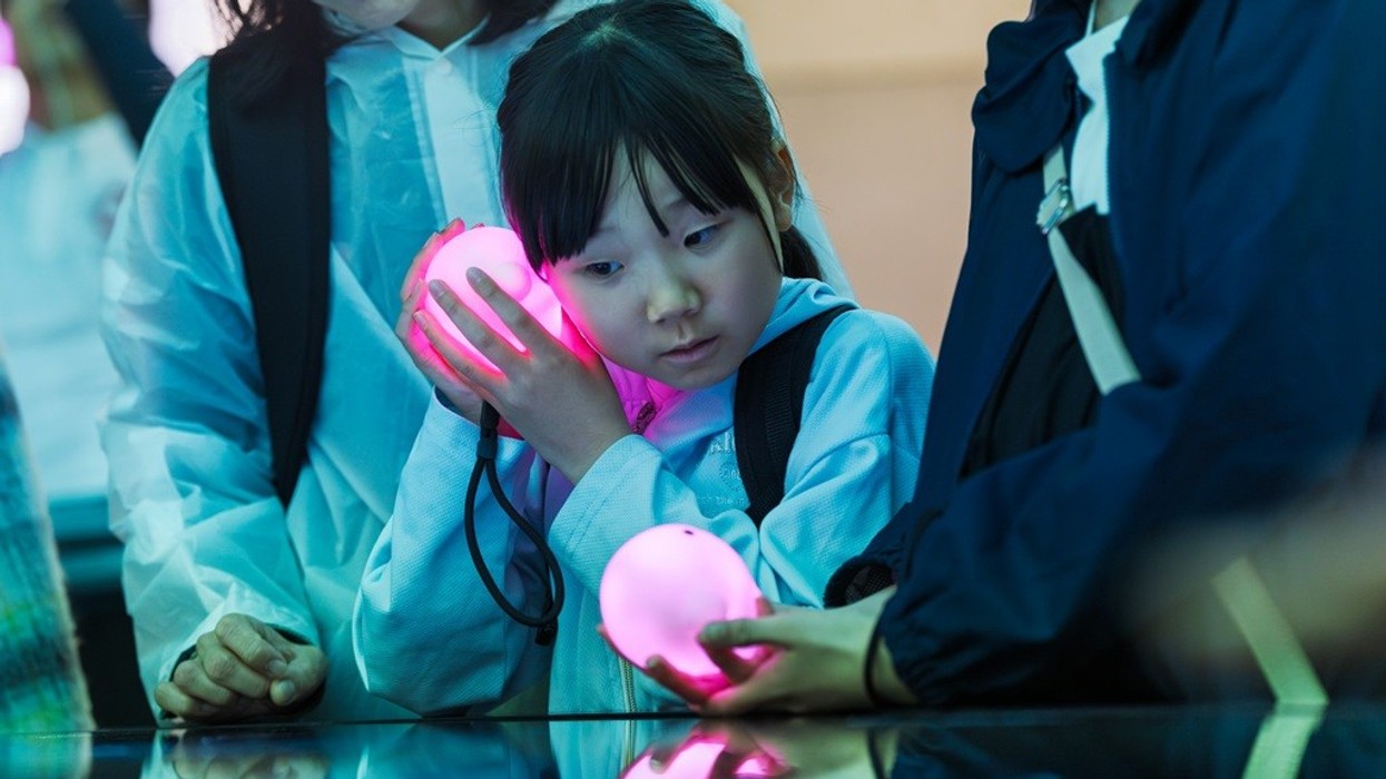 Child holding glowing orb, surrounded by adults in protective clothing at an interactive exhibit.