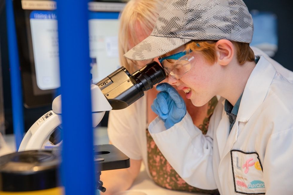 Child in lab coat using a microscope, guided by an adult in the Experiment Zone at the International Centre for Life