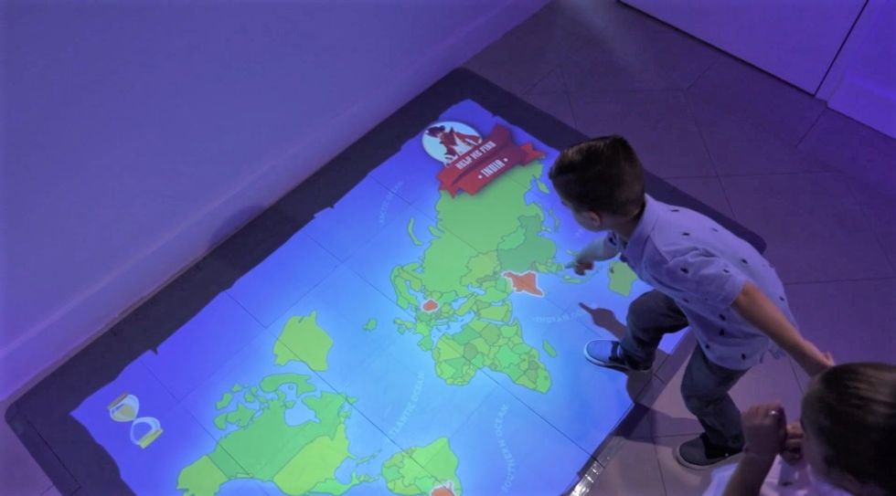 Child interacts with a digital world map projected on the floor, from Breeze Creative