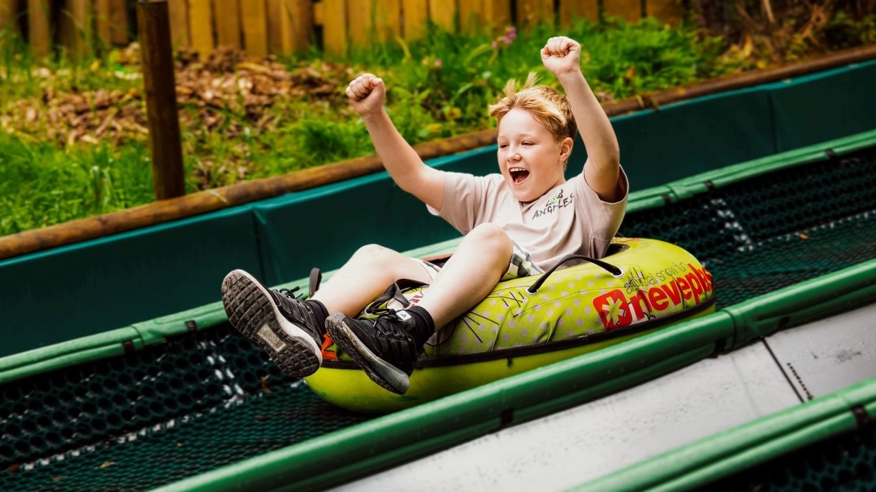 Child joyfully sliding down in a green inflatable tube, arms raised.