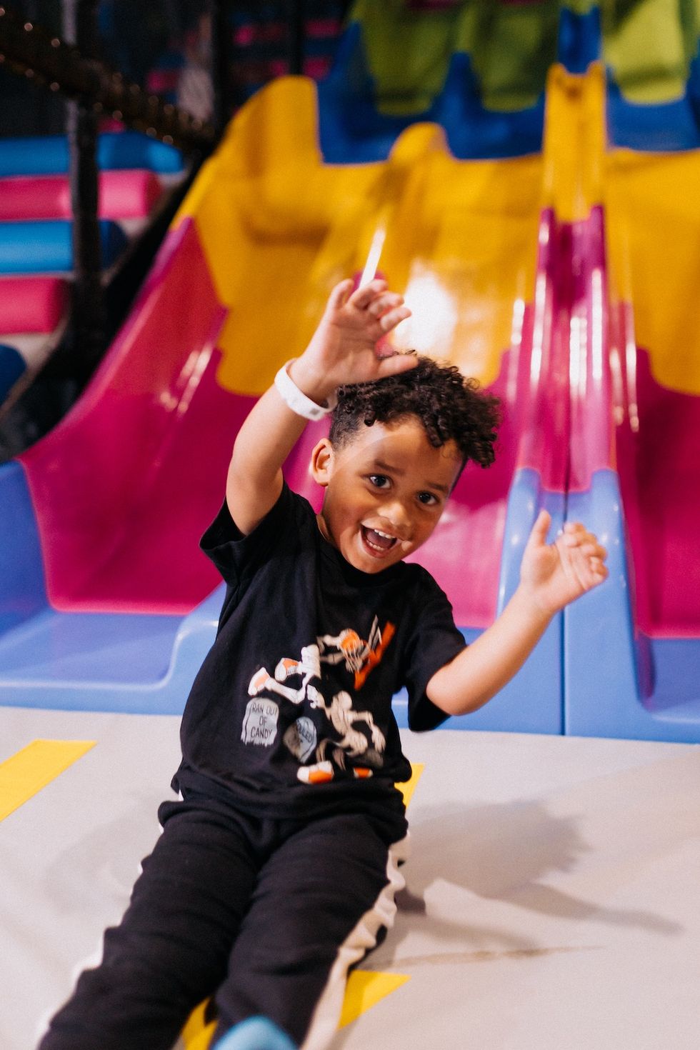 Child laughing on a colorful slide in a play area.