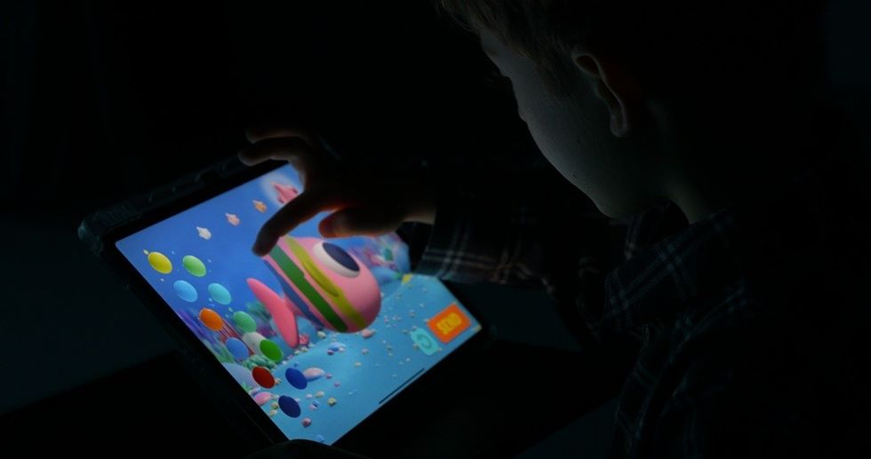 Child playing a colorful game on a tablet in a dimly lit room.
