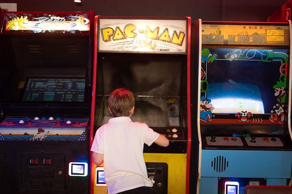 Child playing at a vintage Pac-Man arcade machine at Level Up Arcade, flanked by other classic games.