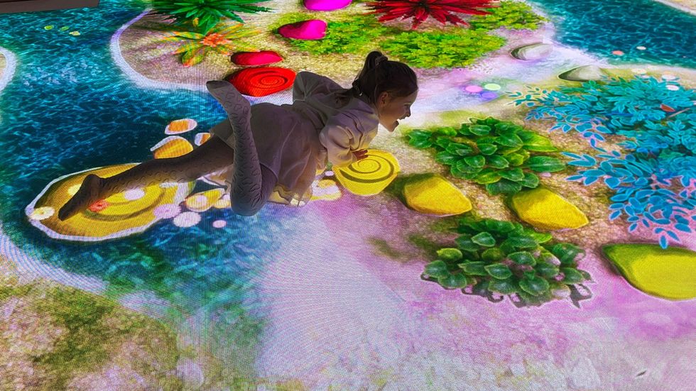 Child playing on vibrant, interactive digital floor with colorful nature-themed graphics.