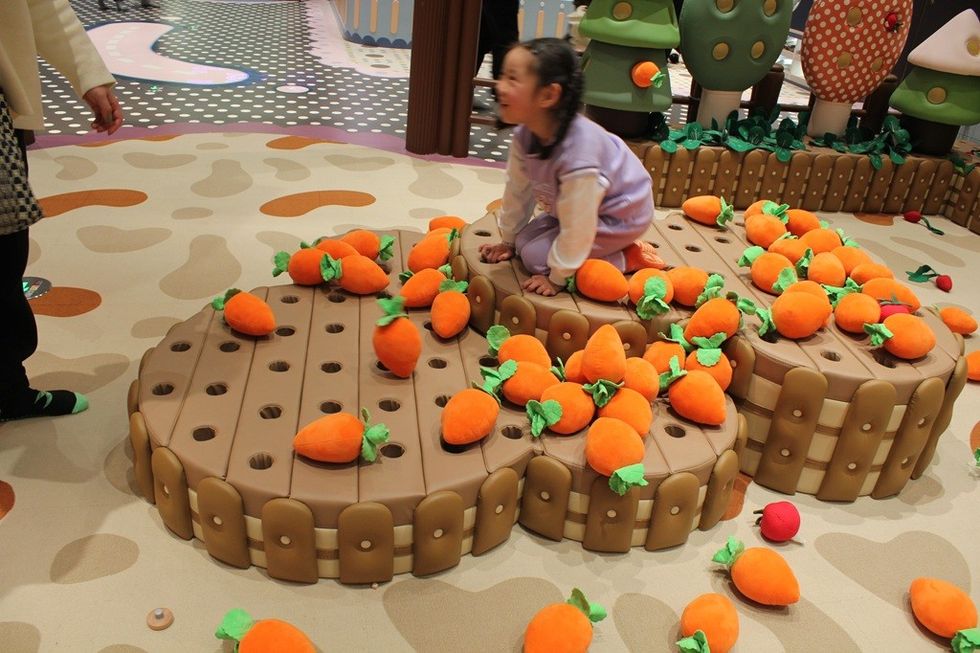 Child playing with soft toy carrots on a play structure indoors.