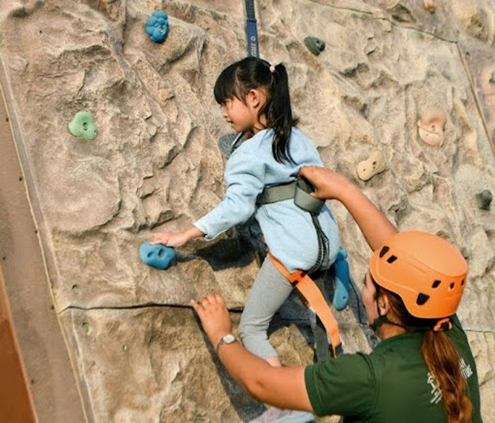 Child rock climbing with assistance from an adult in a helmet at Fujairah Adventure Park