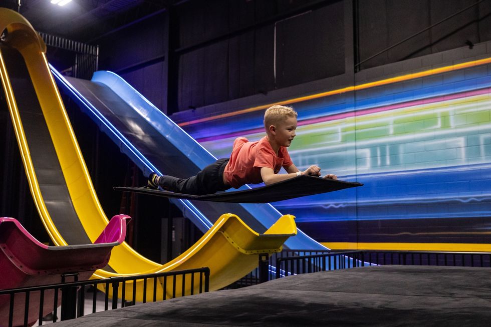 Child sliding on mat in indoor amusement park called Slick City with colorful slides.