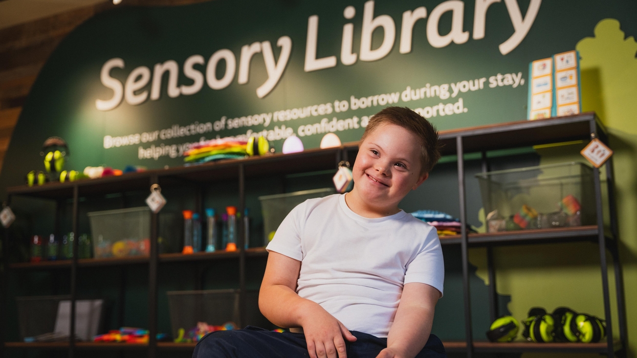 Child smiling in a "Sensory Library" with toys and supplies on shelves behind.