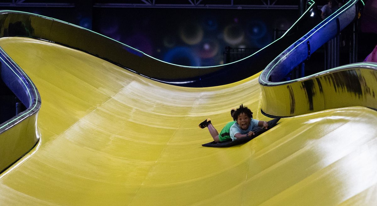 Child smiling while sliding down a large, winding yellow slide on a black mat.