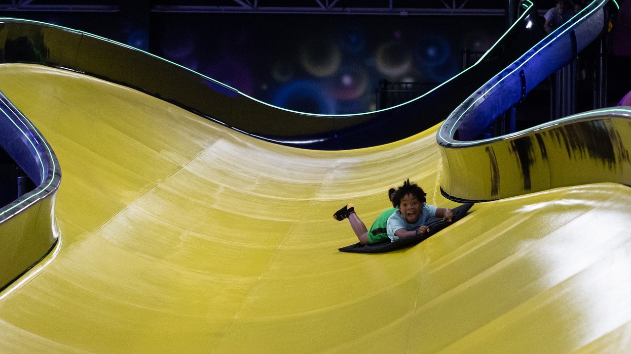 Child smiling while sliding down a large, winding yellow slide on a black mat.