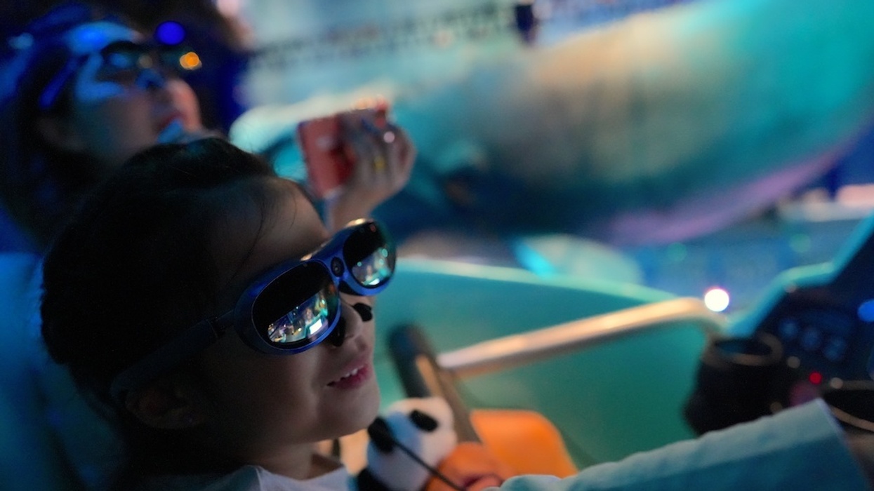 Child wearing 3D glasses, holding a stuffed panda, in an immersive ride experience.