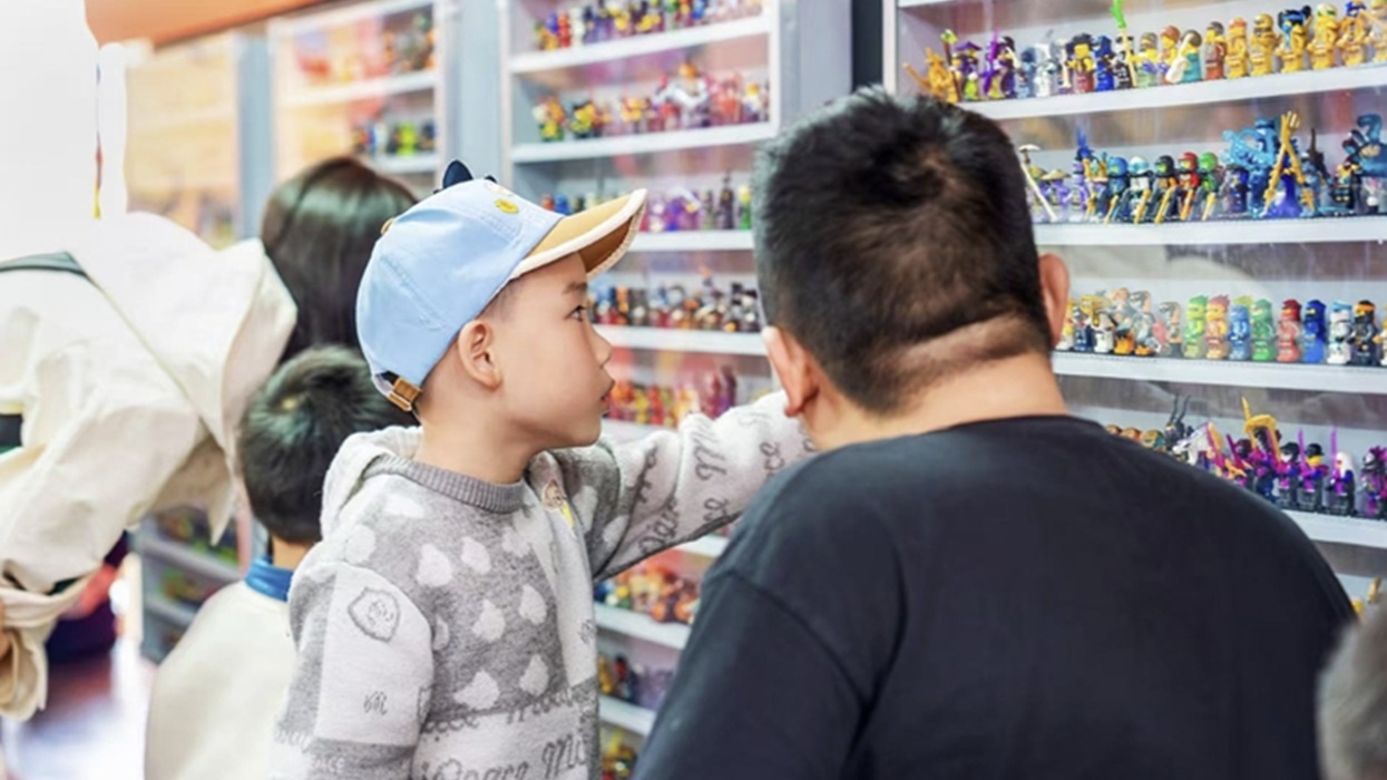 Child wearing blue cap points at toy display case in a Ninjago popup at Legoland.