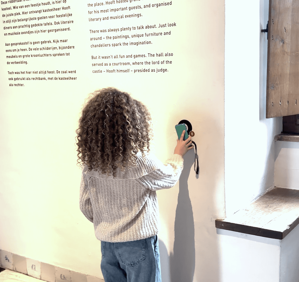 Child with curly hair interacting with a wall display using a device.