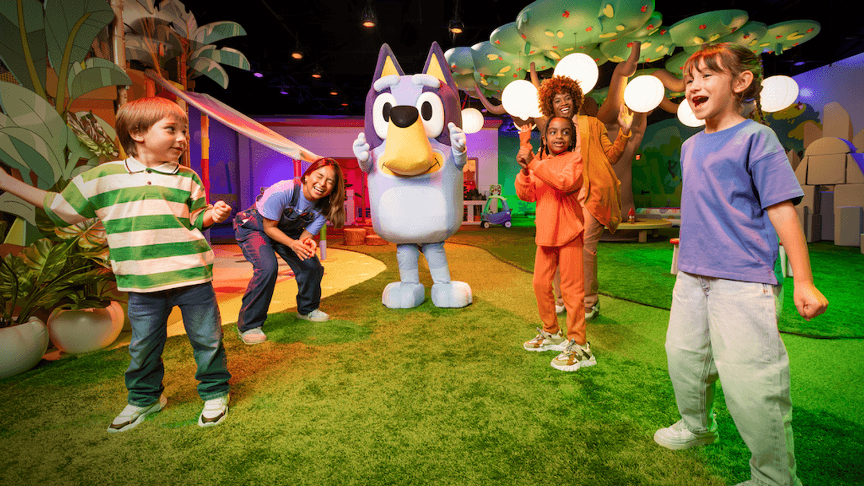 Children and adults playing with a large, blue cartoon character in a colorful indoor playground.