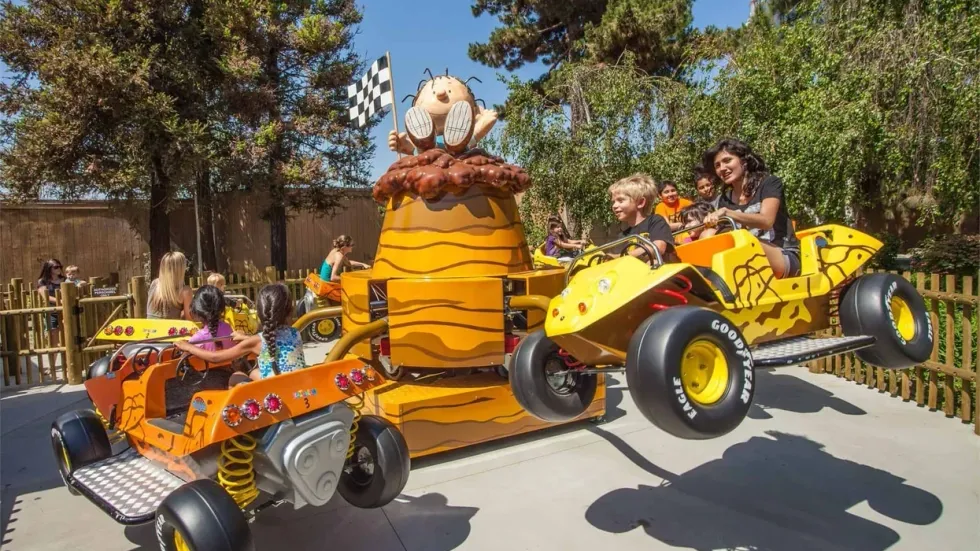 Children enjoy a Peanuts-themed ride with colorful, bee-inspired carriages at an amusement park.