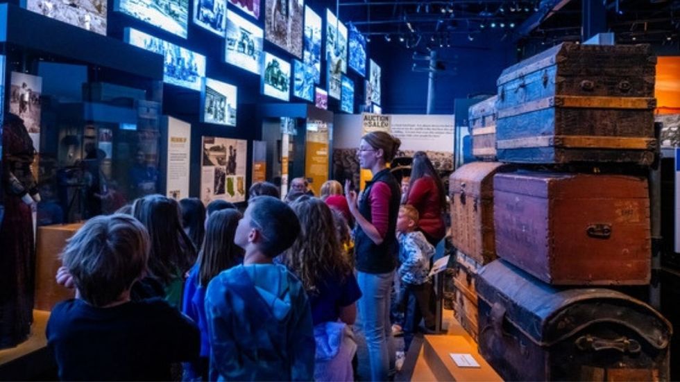 Children exploring a museum exhibit with historic photographs and vintage trunks at Montana Heritage Center.