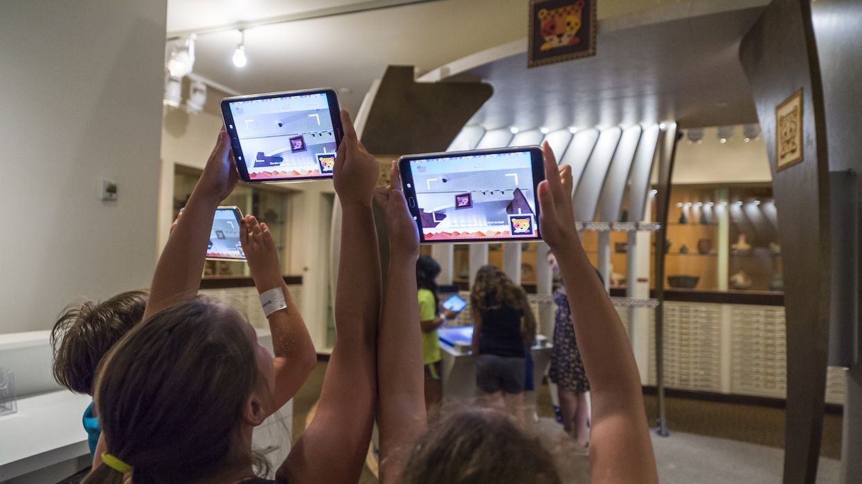 children hold tablets up to museum exhibition