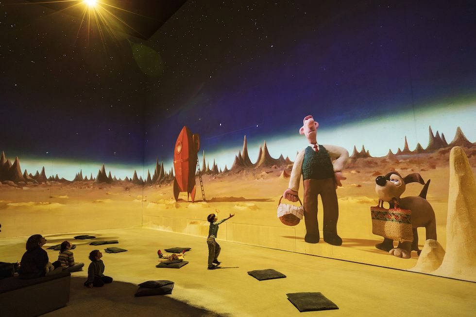 Children interact with a large animated space scene featuring a rocket and characters.