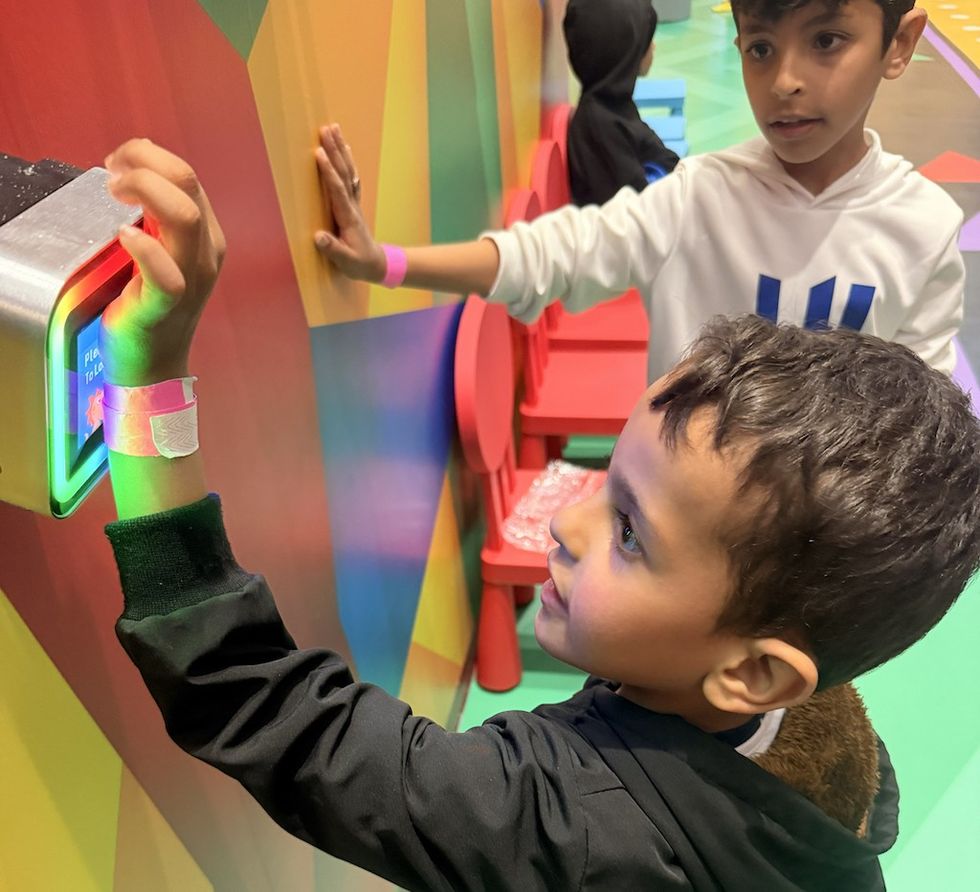 Children interacting with a colorful, lit-up wall display indoors.