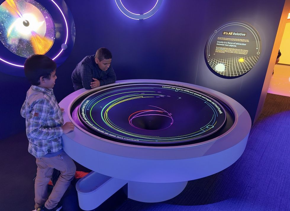 Children interacting with a gravity simulation exhibit featuring neon orbital paths at The Franklin, powered by Beaudry Interactive tech