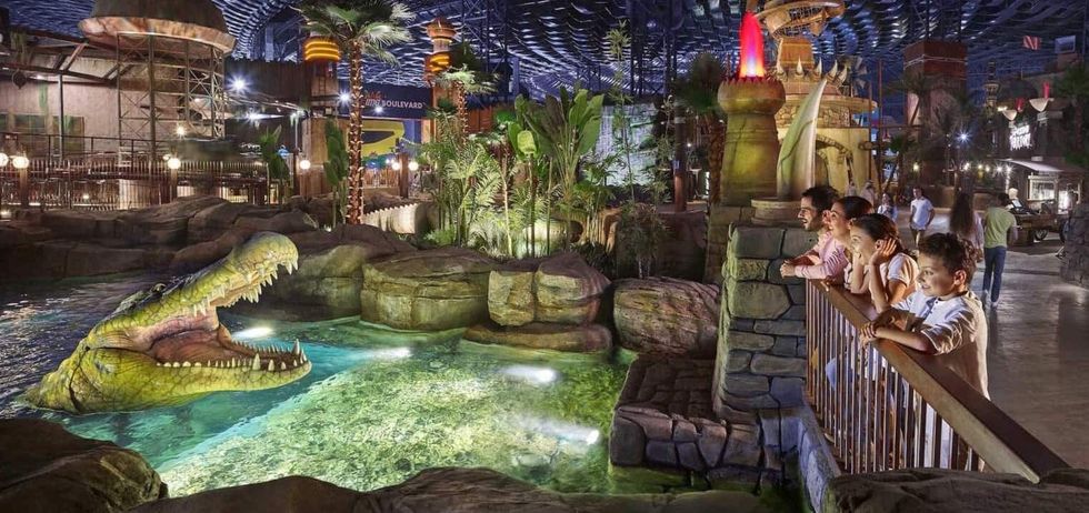 Children observing a lifelike animatronic crocodile in a vibrant indoor theme park.