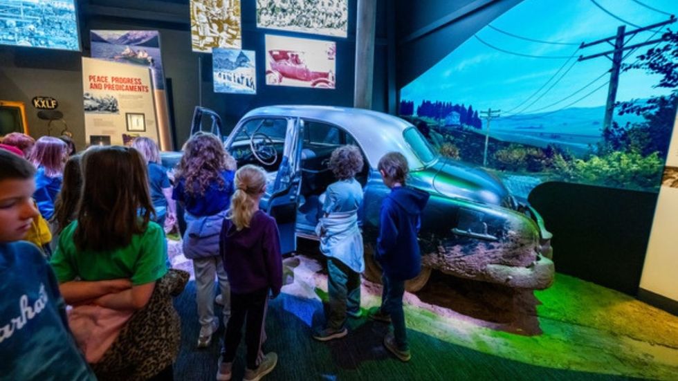 Children observing a vintage car exhibit in a museum display at Montana Heritage Center.