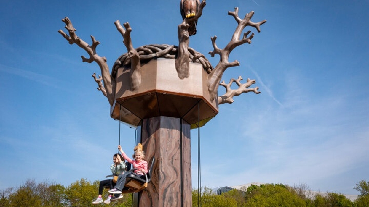 Children on swings attached to a large tree sculpture tower ride from Sunkid with an eagle on top.