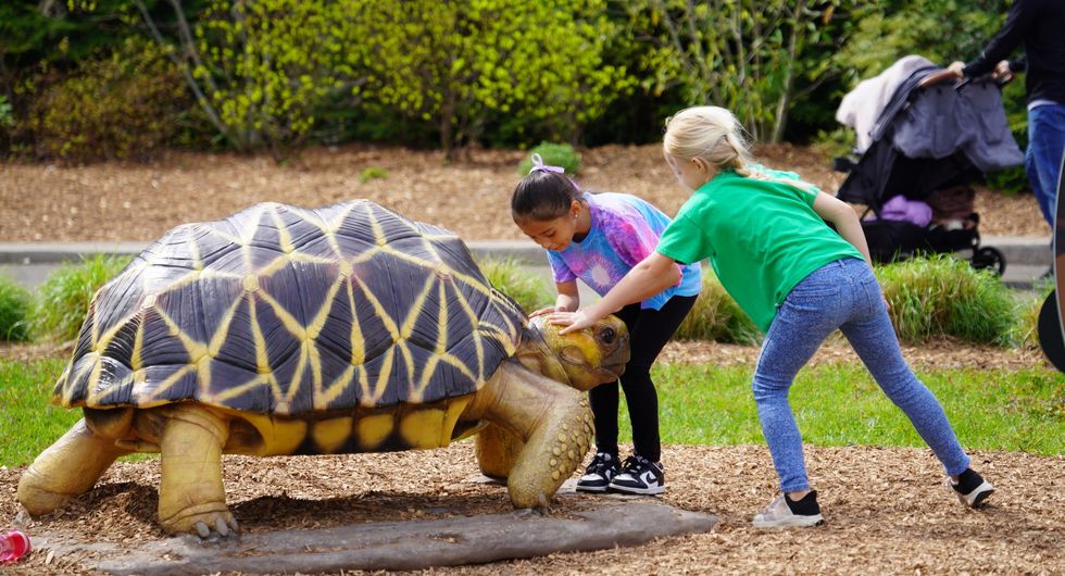 Children petting large tortoise statue in park.