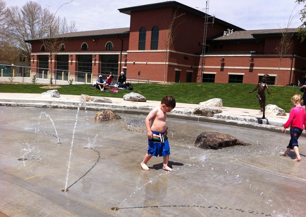 Children play in a shallow fountain area in front of a brick building.