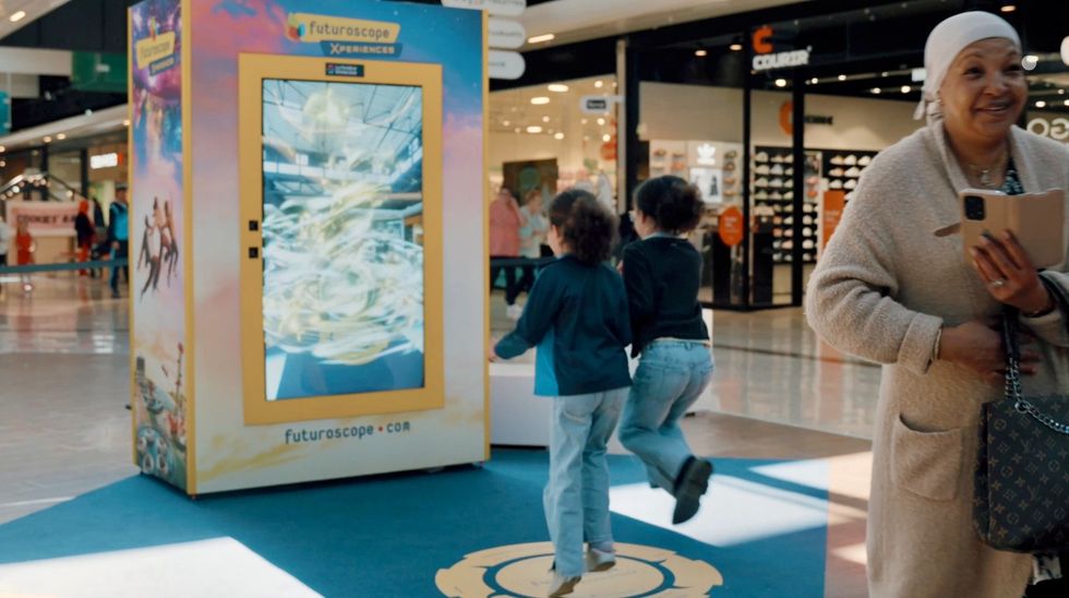 Children play near a large interactive screen in a shopping mall.