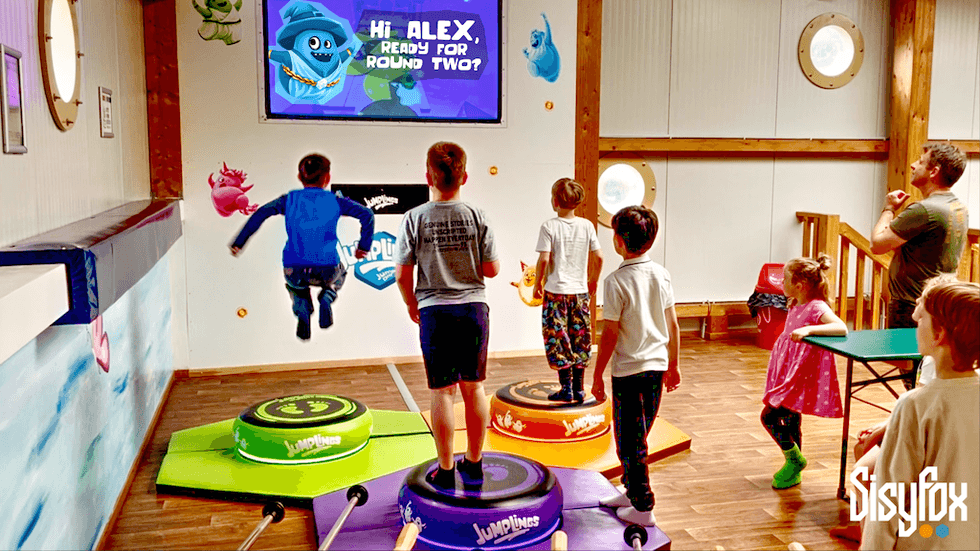 Children playing a digital game from SisyFox with colorful platforms and a screen showing "Ready for Round Two?"