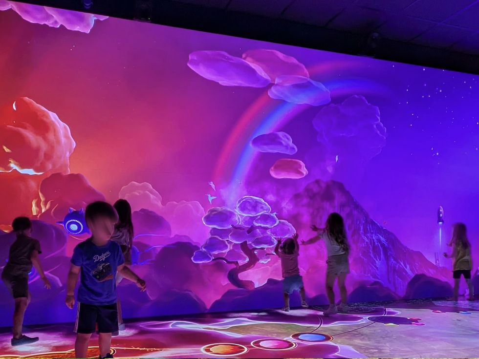Children playing in a colorful, interactive digital landscape with clouds and a rainbow.